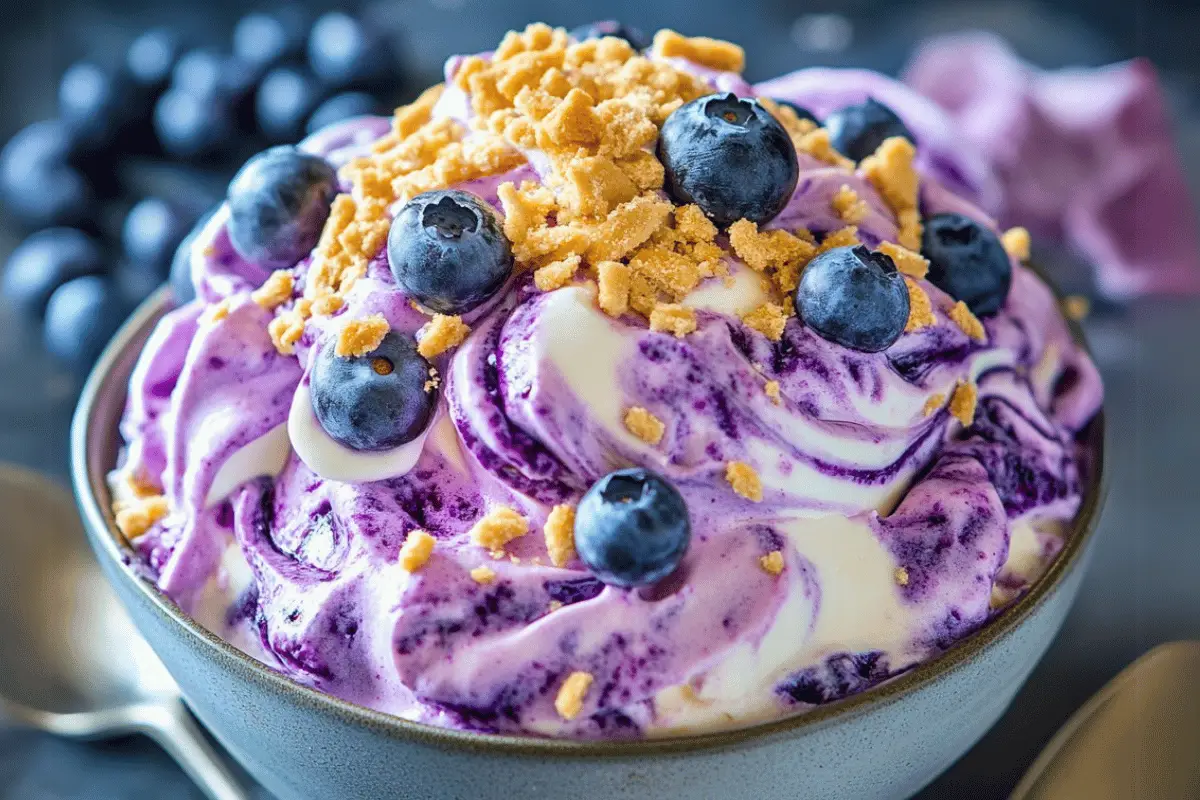 A decorative bowl of Blueberry and Vanilla Cheesecake Fluff topped with fresh blueberries, graham crackers, and mint leaves, set on a festive table.