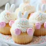 A plate of Bunny Butt Cupcakes decorated with coconut, marshmallow tails, and pink candy feet