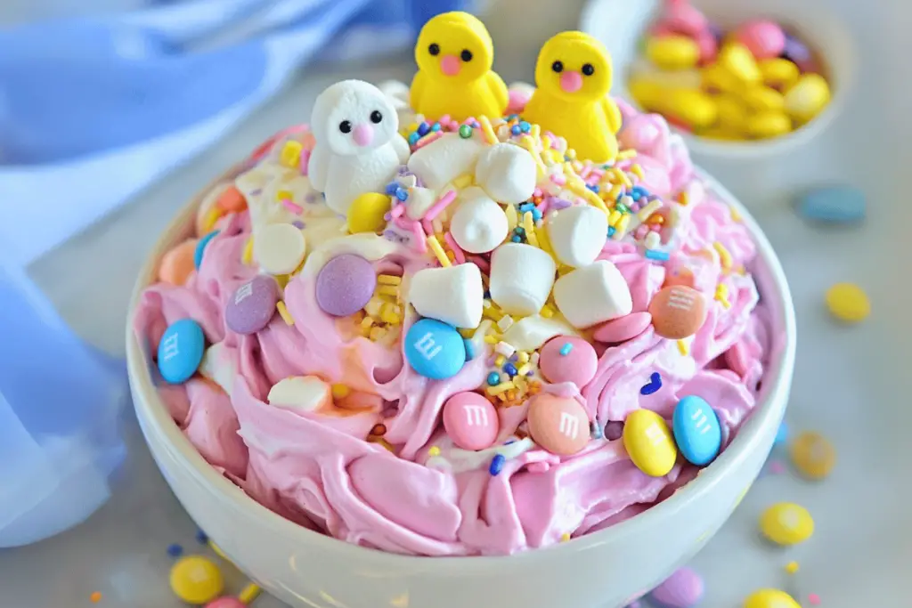 A bowl of pastel-colored Easter Marshmallow Fluff topped with mini marshmallows and chocolate eggs