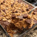 A rich and gooey Peanut Butter Cup Dump Cake topped with melted chocolate and chopped peanut butter cups, served in a baking dish.