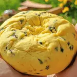 Bright yellow DIY Dandelion Play Dough with fresh flower petals, shaped into balls and flowers on a spring-themed table
